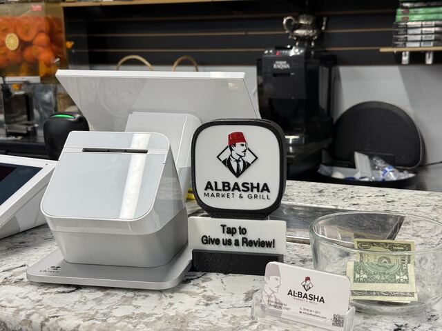 A black TapCraft Stand Pro on the checkout counter at Albasha Market & Grill in Raleigh, next to the card reader and a stack of business cards.