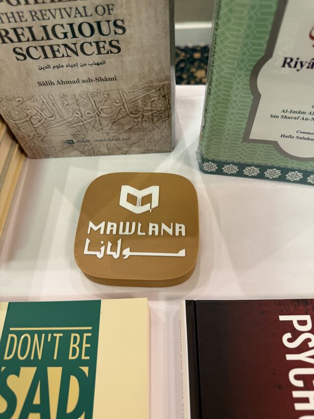 A tan TapCraft display standing on the table at Mawlana's book booth, between stacks of Islamic books.