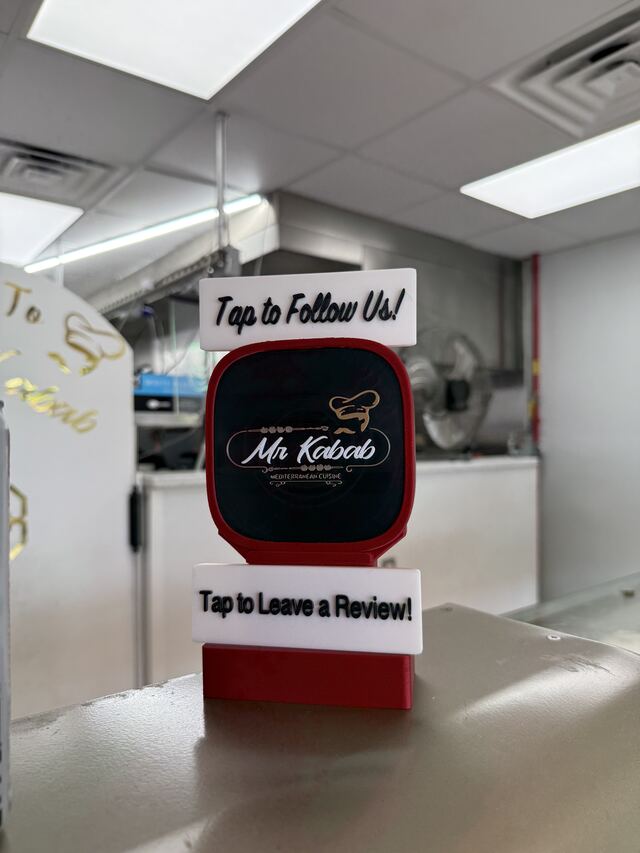 A red TapCraft Stand Pro on the stainless prep counter at Mr. Kabab, with follow and review signs framing the black-and-gold logo.